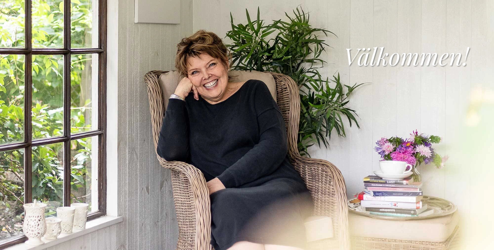 Annelie Ahlmér som sitter i en stol i sitt hus och välkomnar er in.